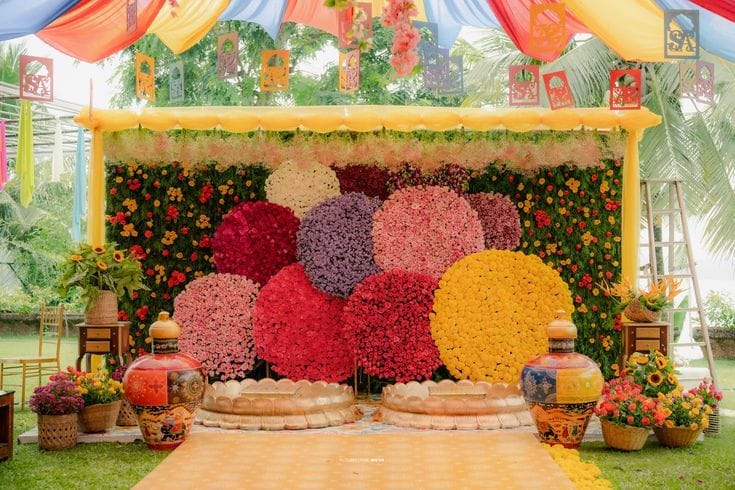 Haldi backdrop of circular flower discs in red, pink and yellow on a green leaf wall by RAW Group
